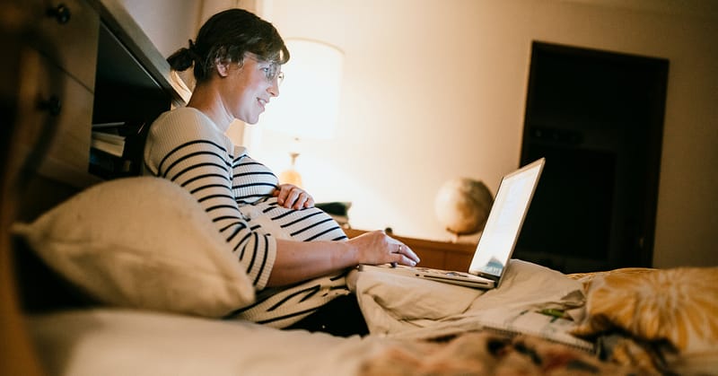 Pregnant person researches on their laptop in bed